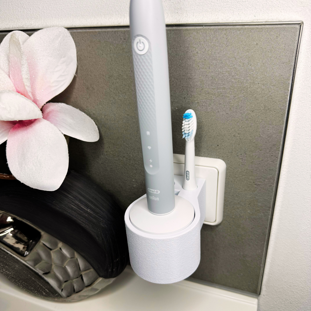 Oral B Pulsonic Slim Clean Zahnbürstenhalterung die direkt in eine Steckdose eingesteckt ist.Die Halterung ist so gestaltet, dass keine Kabel sichtbar sind. Praktische Lösung, um die Zahnbürste aufzubewahren und gleichzeitig den Raum ordentlich zu halten.