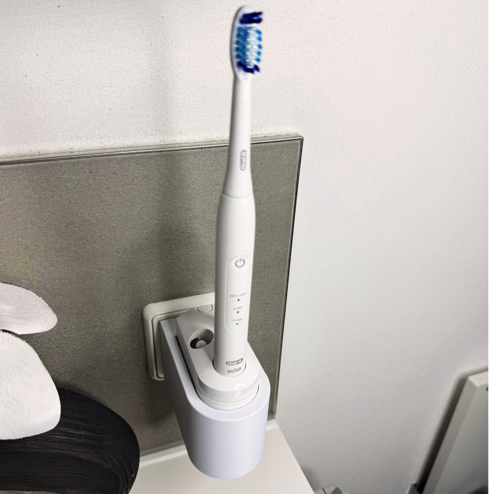 Oral B Pulsonic Smart Zahnbürstenhalterung die direkt in eine Steckdose eingesteckt ist.Die Halterung ist so gestaltet, dass keine Kabel sichtbar sind. Praktische Lösung, um die Zahnbürste aufzubewahren und gleichzeitig den Raum ordentlich zu halten.