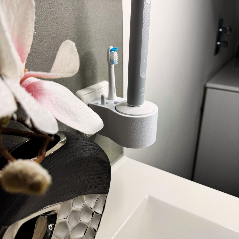 Oral B Pulsonic Slim Clean Zahnbürstenhalterung die direkt in eine Steckdose eingesteckt ist.Die Halterung ist so gestaltet, dass keine Kabel sichtbar sind. Praktische Lösung, um die Zahnbürste aufzubewahren und gleichzeitig den Raum ordentlich zu halten.