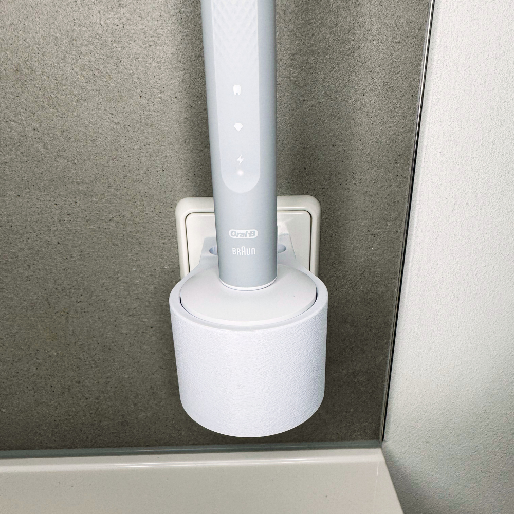 Oral B Pulsonic Slim Clean Zahnbürstenhalterung die direkt in eine Steckdose eingesteckt ist.Die Halterung ist so gestaltet, dass keine Kabel sichtbar sind. Praktische Lösung, um die Zahnbürste aufzubewahren und gleichzeitig den Raum ordentlich zu halten.